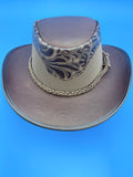 A brown leather cowboy hat with a patterned band and braided rope detail, shown against a solid brown background.