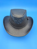A black leather cowboy hat with a textured finish, featuring a patterned black band and braided trim, set against a solid blue background.